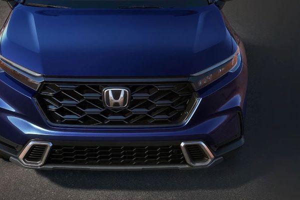 Close-up front view of a blue Honda SUV: Features a black honeycomb grille (Honda logo) and sleek headlights. Polished, modern design highlighted against a dark surface.