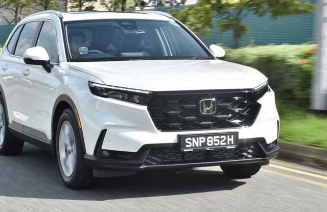 A white Honda SUV driving on a road, with greenery and a blurred background indicating motion, showcasing its sleek front design and dynamic presence.