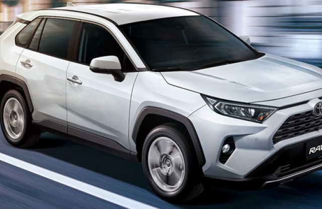 White Toyota RAV4 SUV driving on a road (motion blur effect): features the Toyota logo, "RAV4" badging, and rugged black trim—showcasing its compact crossover design in motion.
