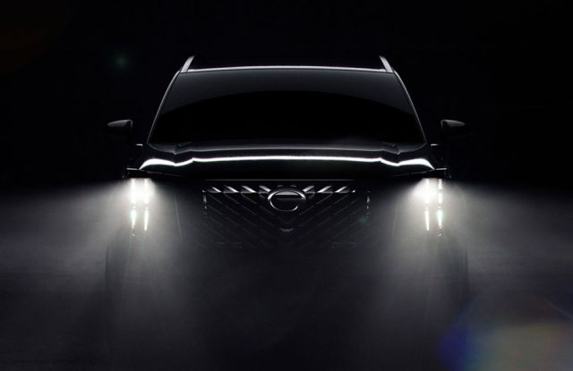 A black SUV with bright headlights on, showcasing a bold grille and logo, set against a dark, misty background for a dramatic effect.