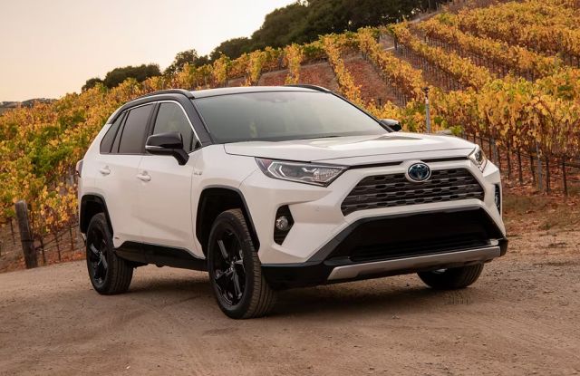 A white Toyota RAV4 SUV parked on a dirt road with a scenic vineyard in the background.