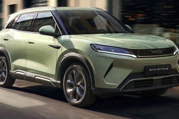 Light green BYD ATTO 2 electric SUV driving on an urban street: features sleek LED headlights, black trim accents, and the "BYD ATTO 2" badge, showcasing its modern, compact design in motion.