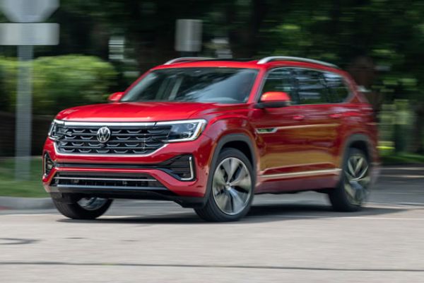 A red Volkswagen SUV driving on a road with greenery and road signs in the background, highlighting its sleek design and dynamic performance.