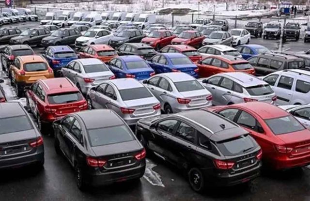 A large parking lot filled with various colored cars, including sedans and SUVs, under a snowy, overcast sky, indicating a busy vehicle storage or dealership area.