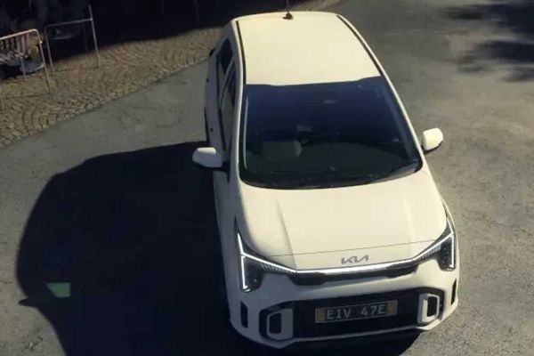 A white Kia car with license plate "E1V 47E" viewed from above, parked on a street near an outdoor café area, highlighting its modern design in an urban setting.