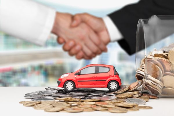 A handshake between two people, a red toy car on a pile of coins, and a jar of coins, symbolizing a car financing or sales agreement.