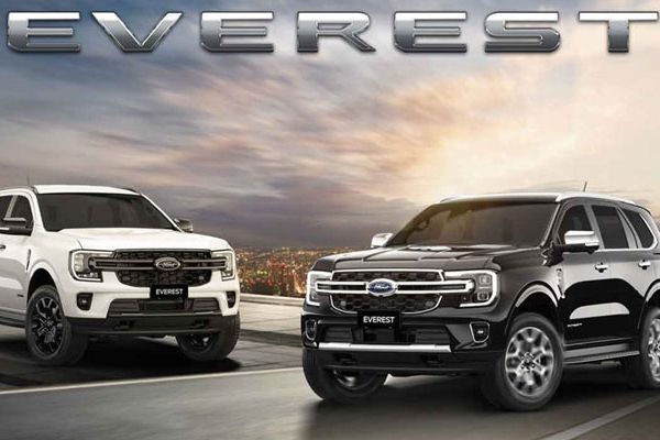 Two Ford Everest SUVs, one white and one black, parked on a road with a city skyline and dramatic sky backdrop, featuring bold "EVEREST" branding.