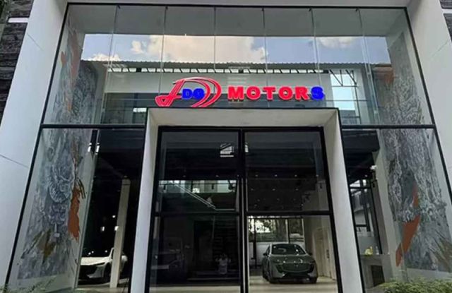 The entrance of DG Motors showroom, featuring a modern glass facade with a colorful logo, and cars visible inside, indicating a sleek automotive dealership.