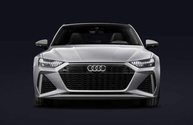 Front view of silver 2026 Audi RS7 (black grille, illuminated lights) against dark, minimalist background.