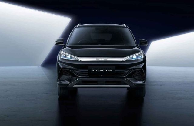 A black BYD Atto 3 SUV showcased from the front in a dramatic, high-contrast studio environment, emphasizing its modern front design and distinctive lighting.