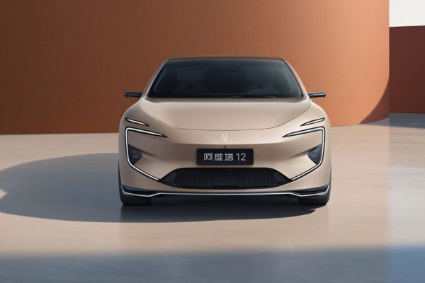 Front view of beige Avatr 12 electric sedan (futuristic lights) parked by terracotta-colored wall.