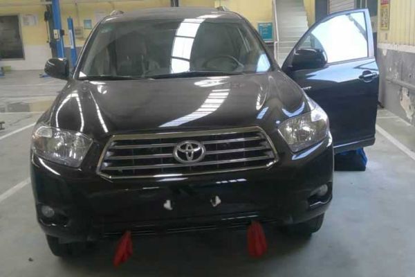 A black Toyota SUV with its driver's door open, parked in an auto repair shop, featuring visible equipment and a clean, spacious environment, indicating vehicle maintenance or inspection.