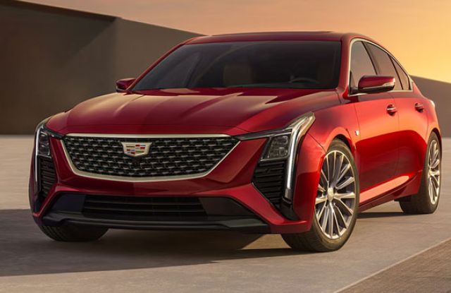 Red Cadillac sedan parked on a smooth surface at sunset: features the brand’s emblem on a black grille, sleek LED headlights, and alloy wheels—showcasing its modern premium design.
