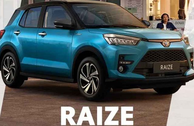 A blue Toyota Raize compact SUV, displayed with its name prominently below, in an urban setting with a café and people in the background, highlighting its stylish design.