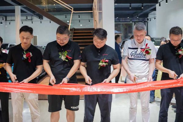A group of people participating in a ribbon - cutting ceremony, likely for a business opening, with a red ribbon and floral decorations.