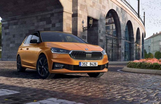 An orange Skoda hatchback parked on a cobblestone street under a historic stone bridge, with a picturesque cityscape in the background, highlighting its stylish design.