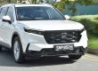 A white Honda SUV driving on a road, with greenery and a blurred background indicating motion, showcasing its sleek front design and dynamic presence.