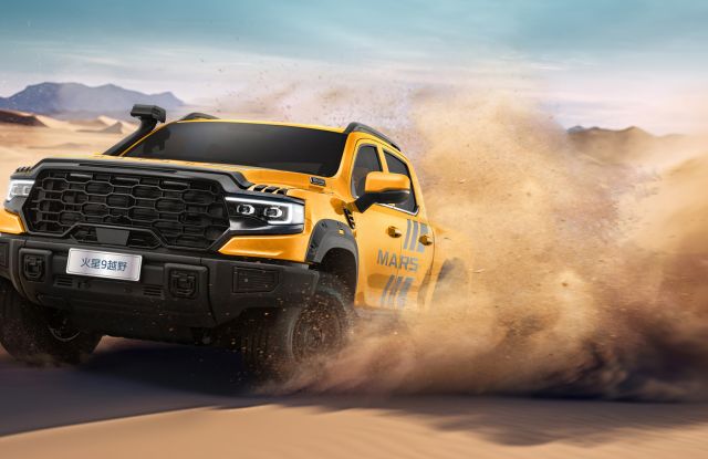 រថយន្តប៊ីកក-up បើកក្រៅផ្លូវពណ៌លឿងឈ្មោះ "Mars 9" កំពុងបើកចរ្យក្នុងទីវាលខ្សាច់ បង្កើតធូលីខ្សាច់ហុយ