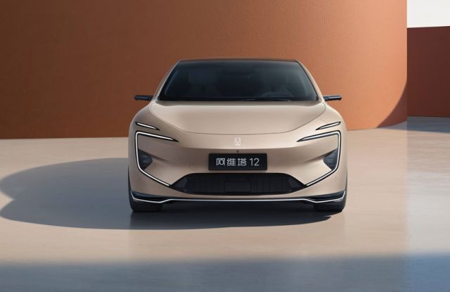 Front view of beige Avatr 12 electric sedan (futuristic lights) parked by terracotta-colored wall.