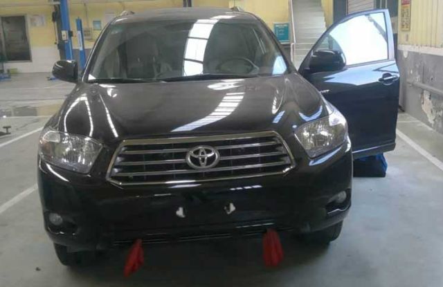 A black Toyota SUV with its driver's door open, parked in an auto repair shop, featuring visible equipment and a clean, spacious environment, indicating vehicle maintenance or inspection.