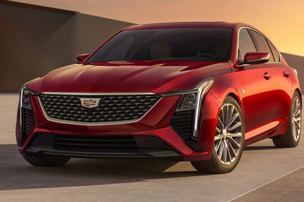 Red Cadillac sedan parked on a smooth surface at sunset: features the brand’s emblem on a black grille, sleek LED headlights, and alloy wheels—showcasing its modern premium design.