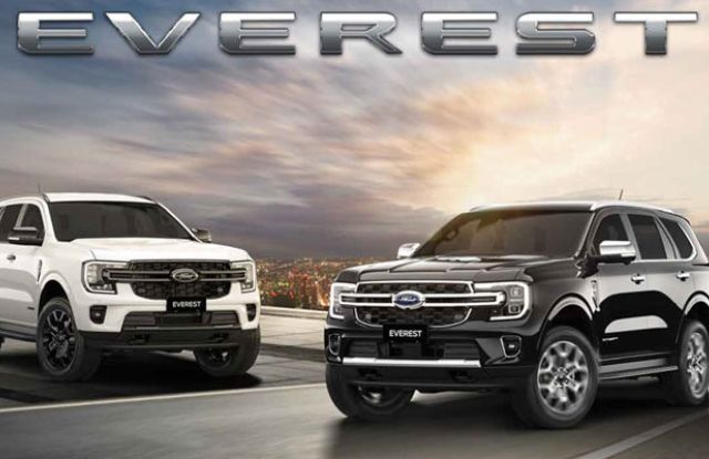 Two Ford Everest SUVs, one white and one black, parked on a road with a city skyline and dramatic sky backdrop, featuring bold "EVEREST" branding.