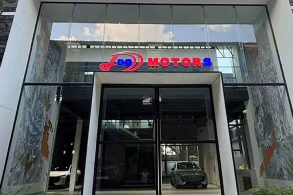 The entrance of DG Motors showroom, featuring a modern glass facade with a colorful logo, and cars visible inside, indicating a sleek automotive dealership.