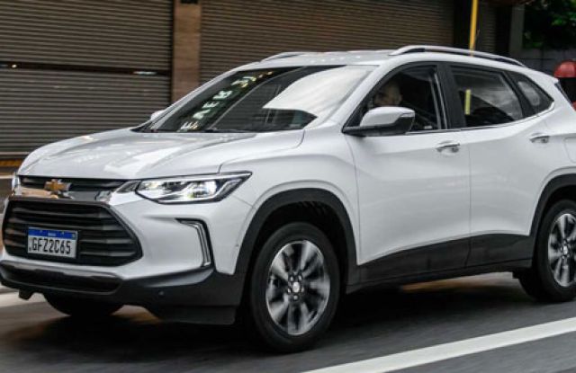 A white Chevrolet SUV driving on a city road, with a license plate "GFZ-2265" and urban buildings in the background.