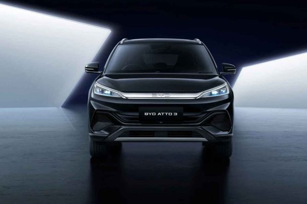 A black BYD Atto 3 SUV showcased from the front in a dramatic, high-contrast studio environment, emphasizing its modern front design and distinctive lighting.