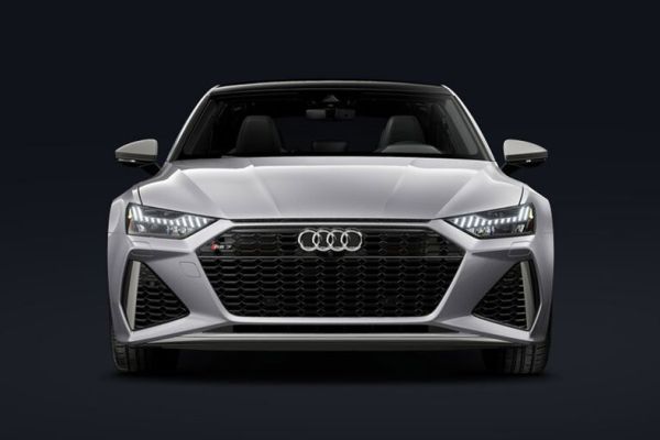 Front view of silver 2026 Audi RS7 (black grille, illuminated lights) against dark, minimalist background.