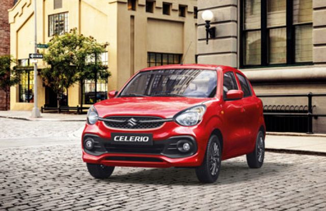 Red Suzuki Celerio parked on a cobblestone street in front of historic city buildings.