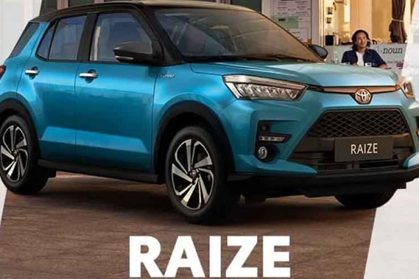 A blue Toyota Raize compact SUV, displayed with its name prominently below, in an urban setting with a café and people in the background, highlighting its stylish design.