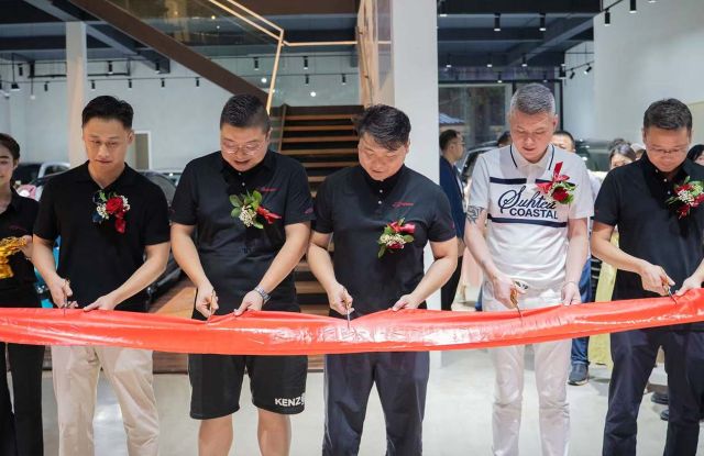 A group of people participating in a ribbon - cutting ceremony, likely for a business opening, with a red ribbon and floral decorations.