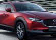Red Mazda CX-30 crossover: Features Mazda logo, "MAZDA CX-30" badging, sleek headlights, and dual-tone alloy wheels—displayed by a modern building, showcasing its sporty design.