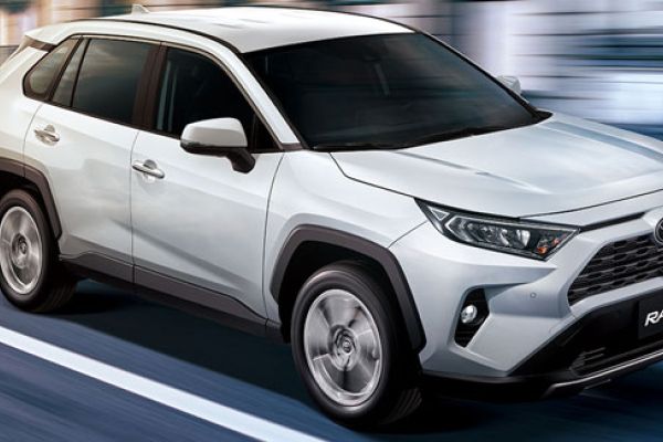 White Toyota RAV4 SUV driving on a road (motion blur effect): features the Toyota logo, "RAV4" badging, and rugged black trim—showcasing its compact crossover design in motion.