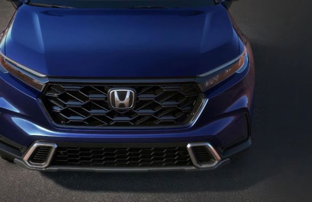 Close-up front view of a blue Honda SUV: Features a black honeycomb grille (Honda logo) and sleek headlights. Polished, modern design highlighted against a dark surface.