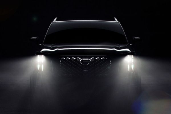 A black SUV with bright headlights on, showcasing a bold grille and logo, set against a dark, misty background for a dramatic effect.