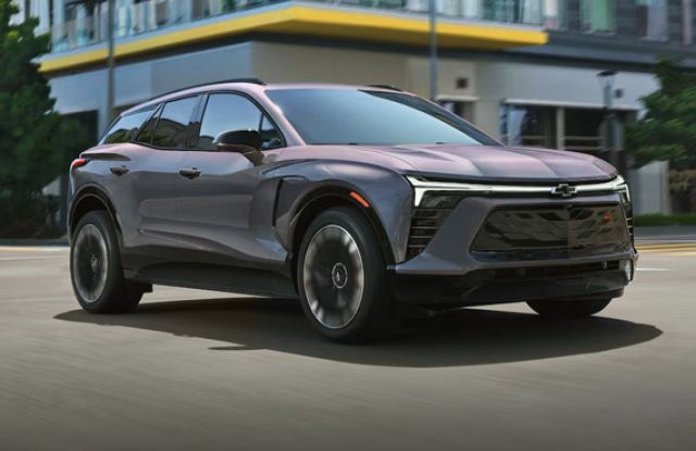 Sleek gray Chevrolet electric SUV driving on a city street, featuring sharp, futuristic LED headlights.