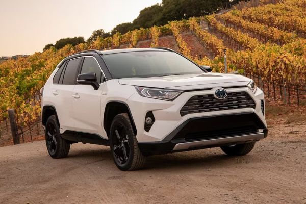 A white Toyota RAV4 SUV parked on a dirt road with a scenic vineyard in the background.
