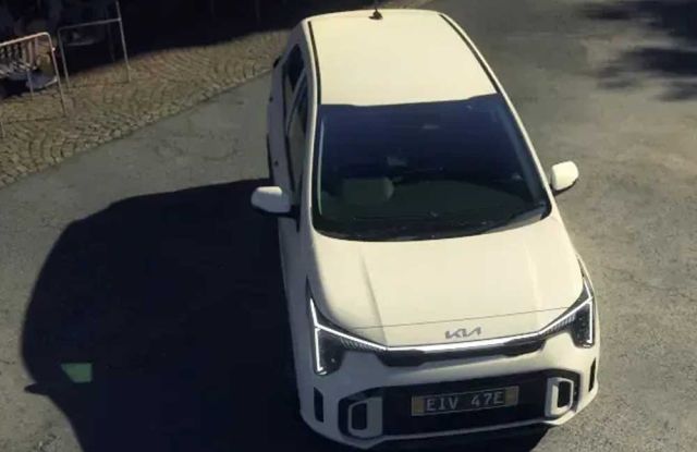 A white Kia car with license plate "E1V 47E" viewed from above, parked on a street near an outdoor café area, highlighting its modern design in an urban setting.