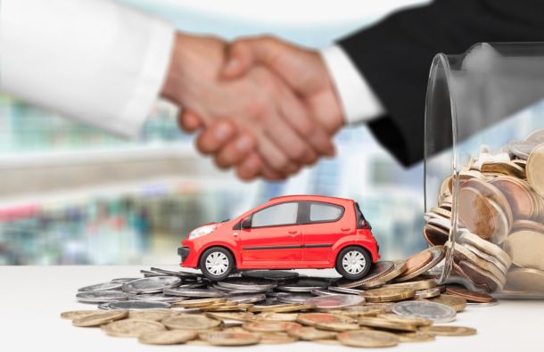 A handshake between two people, a red toy car on a pile of coins, and a jar of coins, symbolizing a car financing or sales agreement.