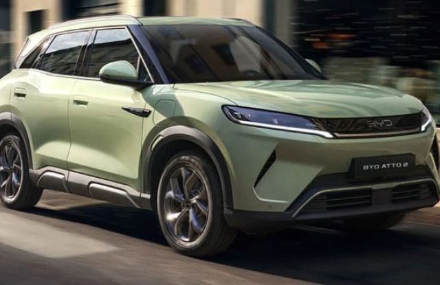 Light green BYD ATTO 2 electric SUV driving on an urban street: features sleek LED headlights, black trim accents, and the "BYD ATTO 2" badge, showcasing its modern, compact design in motion.