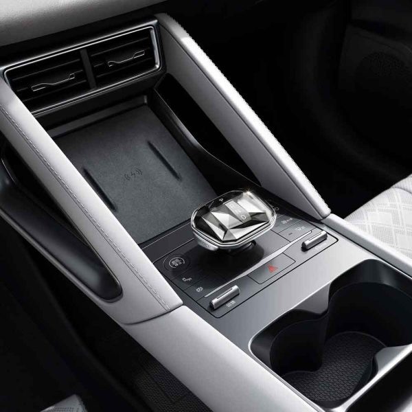 Close - up of a car's center console, featuring a crystal - like gear shifter, wireless charging pad, and cup holders.