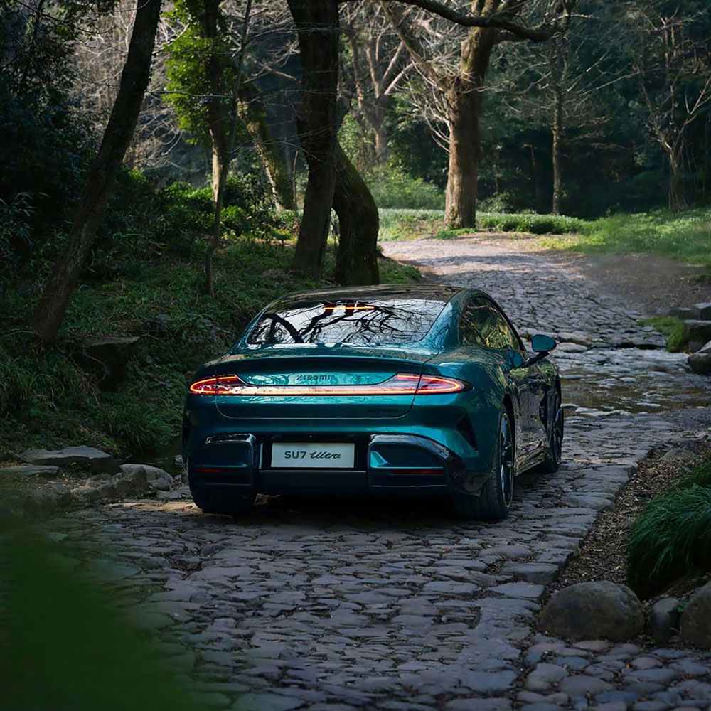 Rear view of a teal SU7 Ultra car on a cobblestone road in a wooded area.