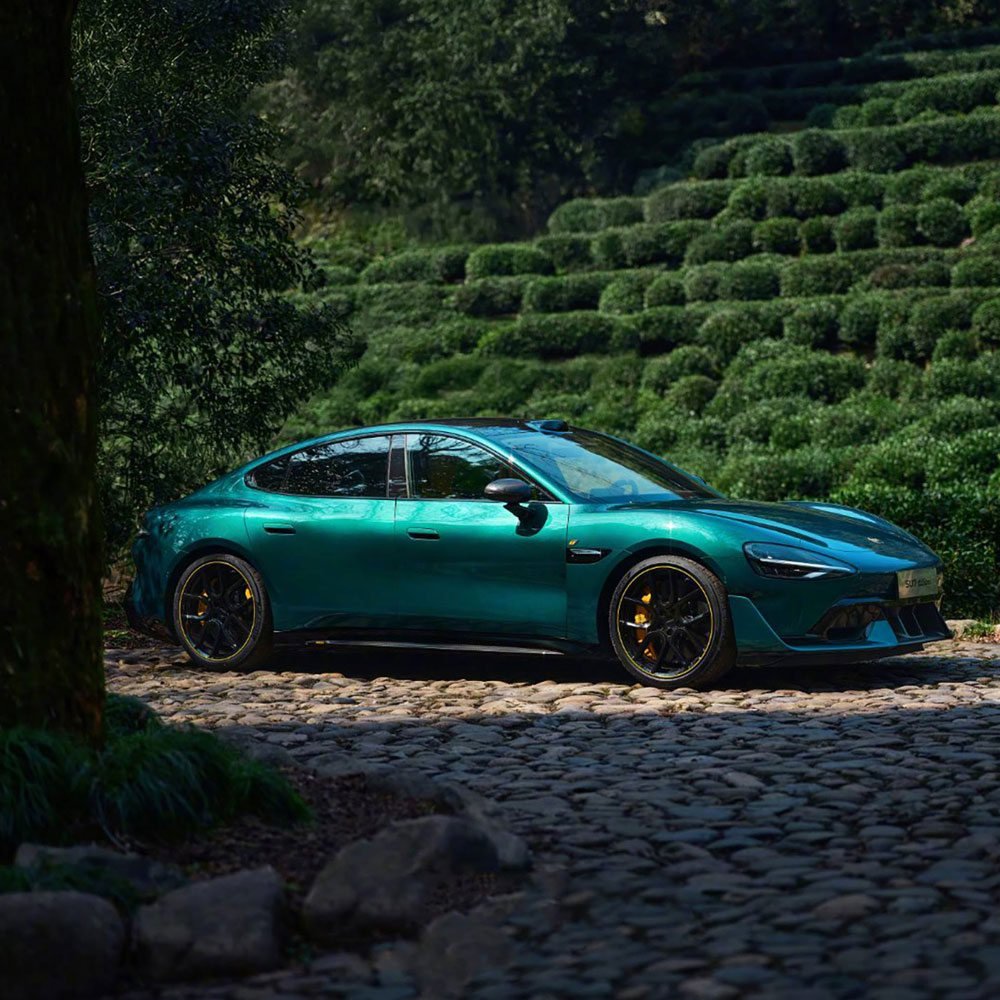 A teal sports car parked on a cobblestone road in a lush, green mountainous area.