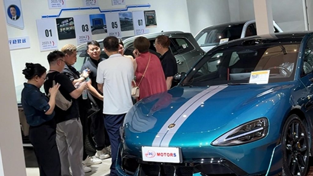 People gather around cars at an auto showroom, discussing with a salesperson.