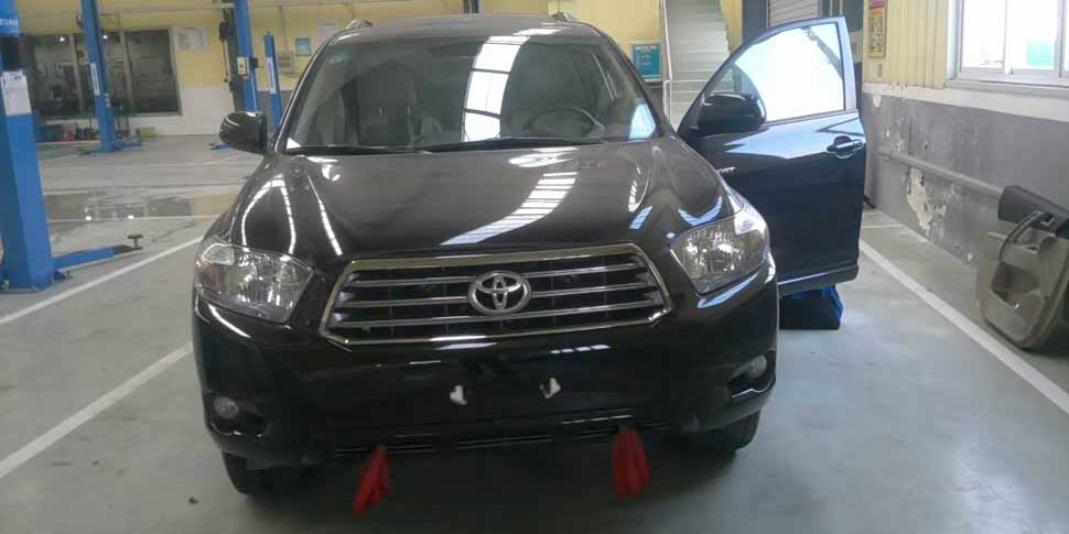 A black Toyota SUV with its driver's door open, parked in an auto repair shop, featuring visible equipment and a clean, spacious environment, indicating vehicle maintenance or inspection.