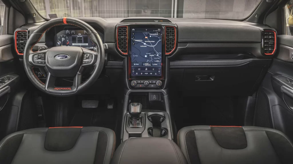 Interior of a Ford vehicle, featuring a steering wheel, a central touchscreen with a map, and black seats with orange accents.