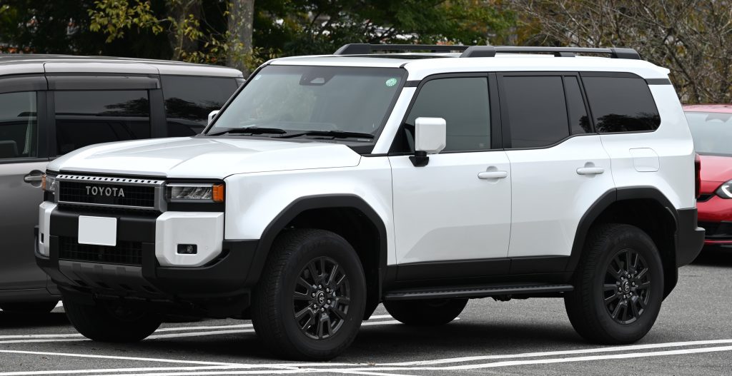 A white Toyota SUV parked in a parking lot with other vehicles and trees in the background.