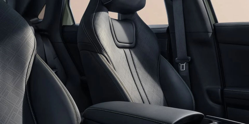 Close-up of a car's black front seat: textured fabric with stitched detailing, integrated headrest, and adjacent armrest—showcasing the cabin's premium, ergonomic seating design.